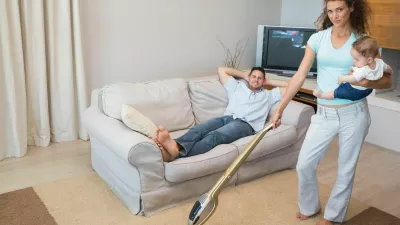 ženska čisti, čiščenje, pospravljanje, gospodinjska dela Full length portrait of woman cleaning house while carrying baby with man relaxing on sofa,Image: 184546642, License: Royalty-free, Restrictions:, Model Release: yes