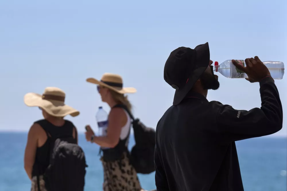 FILE - A tourist drinks water on a hot day at the beach in Barcelona, Spain, July 2, 2025. (AP Photo/Emilio Morenatti, File)