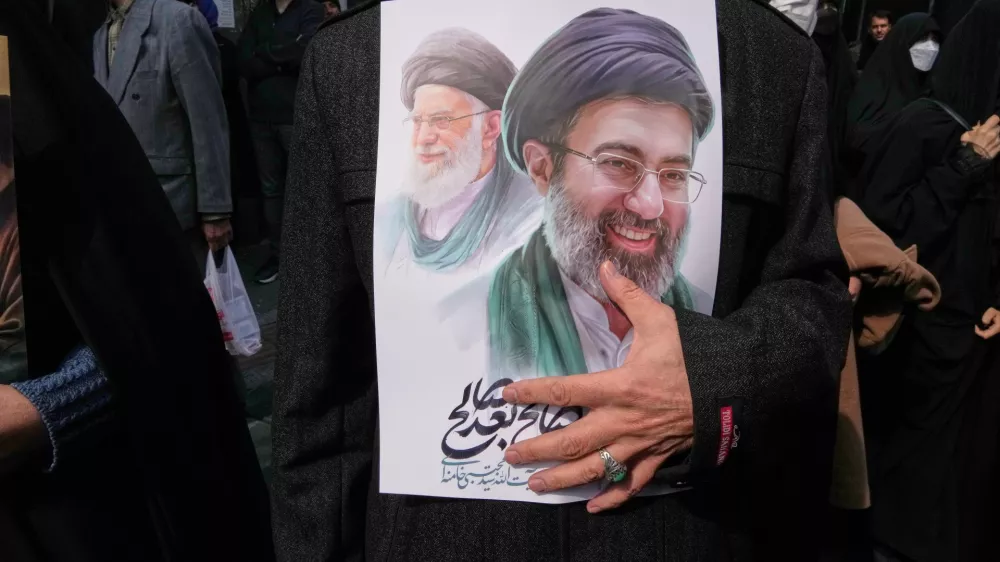 A mourner holds a poster depicting Ayatollah Mojtaba Khamenei, right, the successor to his late father Ayatollah Ali Khamenei, left, as supreme leader, during the funeral procession for senior Iranian military officials and civilians killed during the U.S.-Israel campaign in Tehran, Iran, Wednesday, March 11, 2026. (AP Photo/Vahid Salemi)