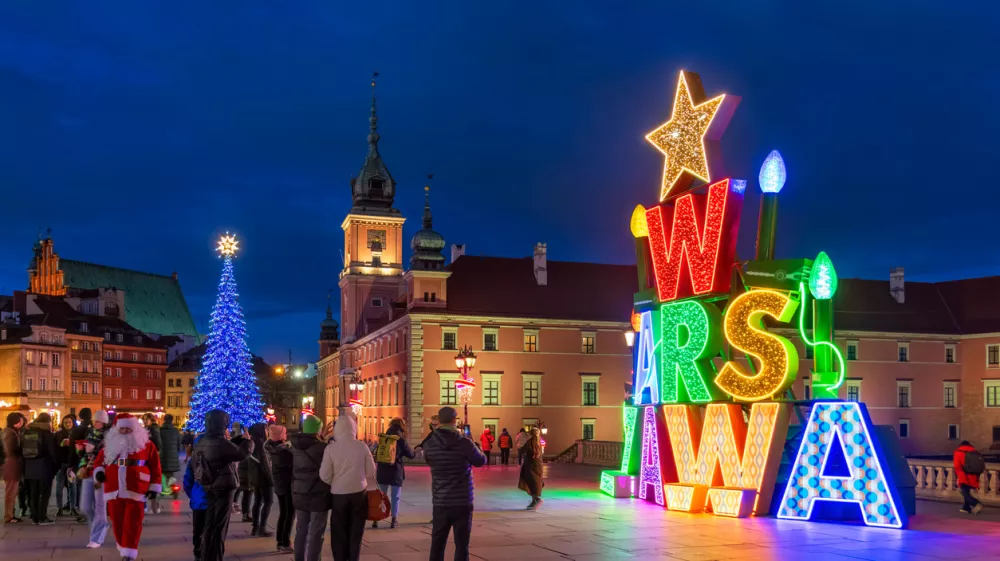 Warsaw, Poland - December 20, 2024: Illuminated Warszawa (Warsaw) sign and group of people on the Castle Square in the Old Town at night, Christmas time holiday season illumination.