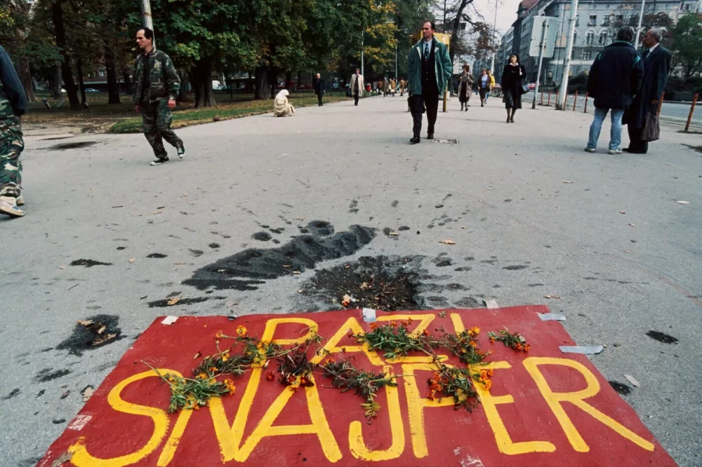 Floral tributes lay on a poster reading "Beware of Snipers" placed next to a mortar grenade crater in Sarajevo on November 01 1995, as residents walk past on All Saints Day. The poster was placed here as an All Saints Day monument in order to commemorate the 10.615 people killed in the Bosnian capital during the war. AFP PHOTO,Image: 565576136, License: Rights-managed, Restrictions:, Model Release: no