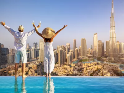 A happy tourist couple on vacation time stands by the pool edge and enjoys the panoramic sunset view of the Dubai city skyline, UAE / Foto: Shansche, Getty Images