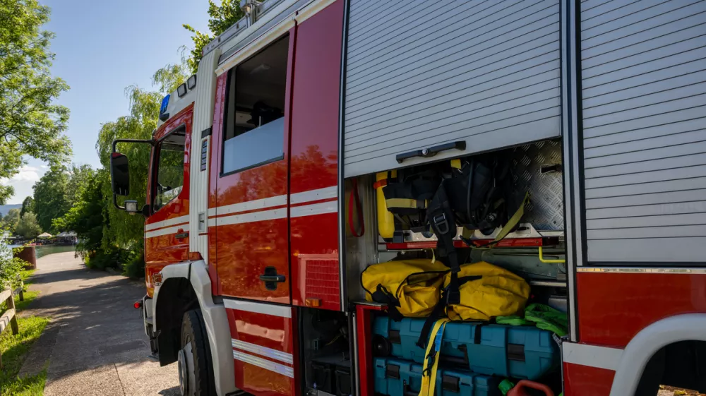 Close-up view of fire truck's open storage compartment revealing organized emergency rescue gear, colorful equipment, and yellow hoses under natural daylight conditions.
