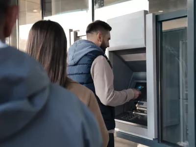 Young man using cash machine for money withdrawal outdoors. ATM queue
