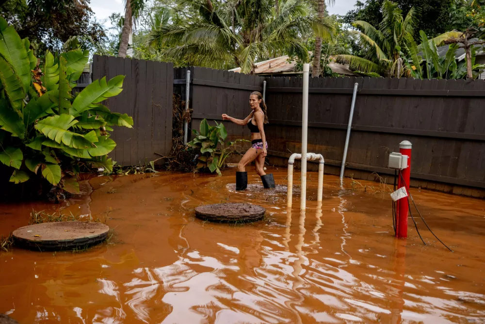 Linda Griffith wades through a flooded yard in Haleiwa, Hawaii Saturday, March 21, 2026. (Stephen Lam/San Francisco Chronicle via AP)