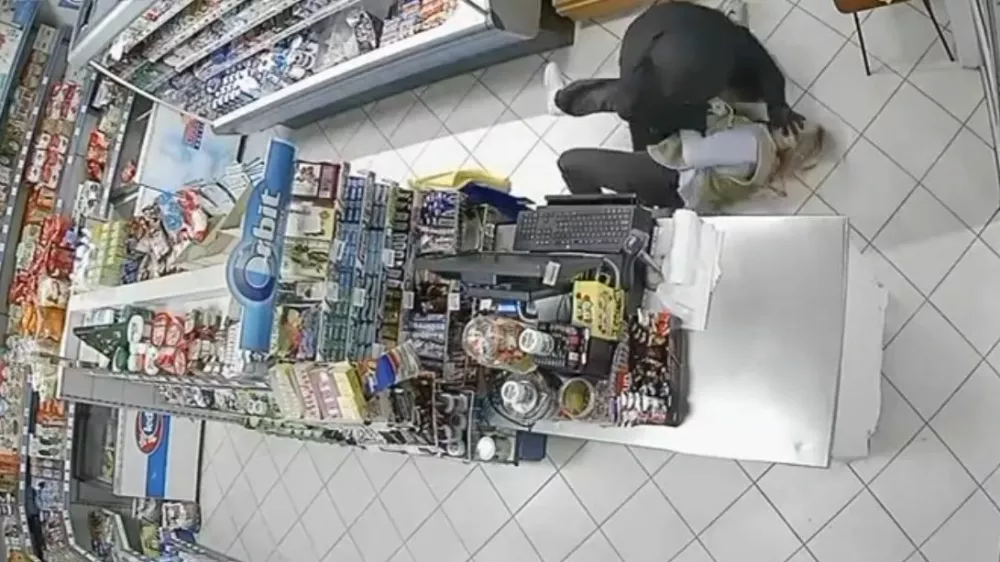 Nesojeni ropar je prodajalko vrgel po tleh in jo tepel, ona pa se je krčevito držala njegovega orožja. 