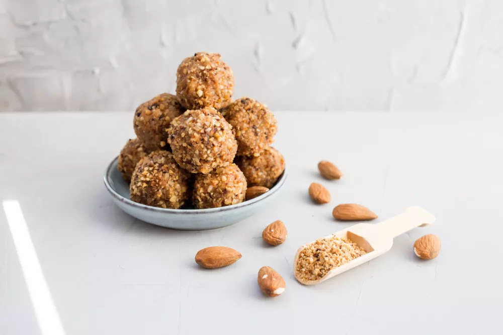 Organic healthy energy balls of dates, peanuts, honey, almonds in walnut chips on a light background, copy the space, lie flat. Healthy food, healthy snack. Raw dessert. Gray background. / Foto: Katsiaryna Voitsik