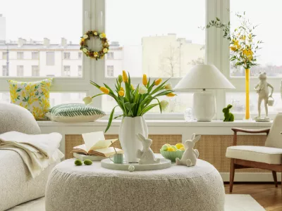 Bright living room with an Easter setup featuring yellow tulips in a white vase, soft textured pillows, and delicate decorations, creating a warm and festive ambiance.