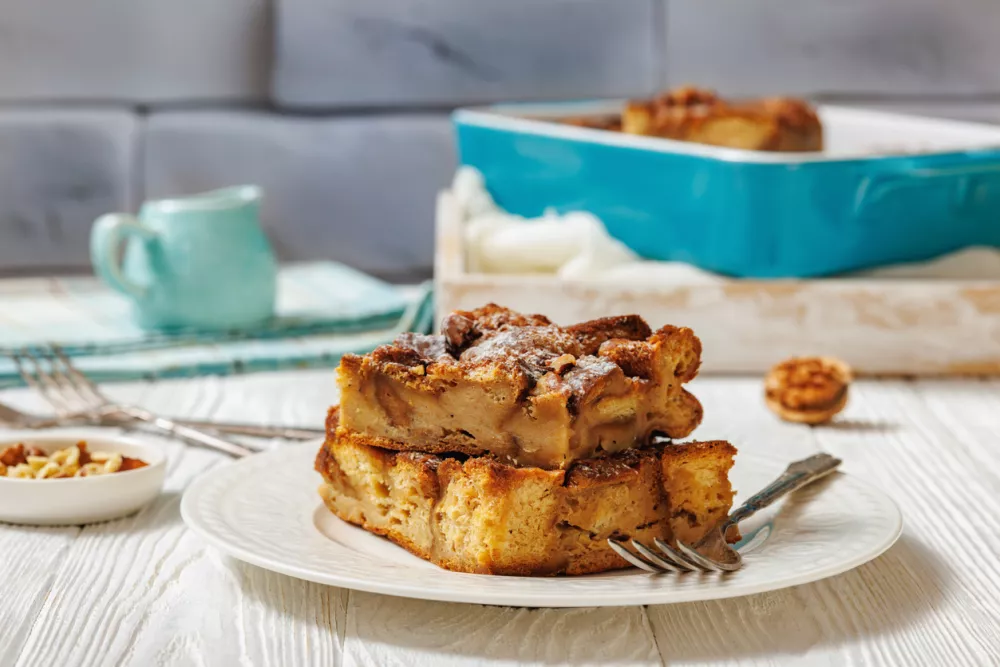 Cinnamon Brioche French Toast Casserole with crunchy walnuts streusel topping on a plate with fork on a white wooden table, horizontal view from above, close-up