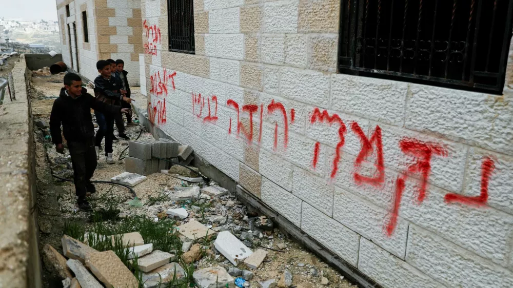 Boys stand near graffiti that reads, "Revenge. Death to Arabs", which Palestinians say was written by Israeli settlers, near Hebron in the Israeli-occupied West Bank, March 30, 2026. REUTERS/Yosri Aljamal