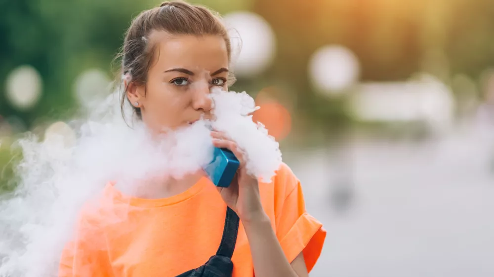 Pretty young girl vape popular ecig gadget,vaping device.Happy brunette vaper girl with e-cig.Portrait of smoker female model with electronic cigarette vaporizer.Ejuice vaping with fruit flavor liquid