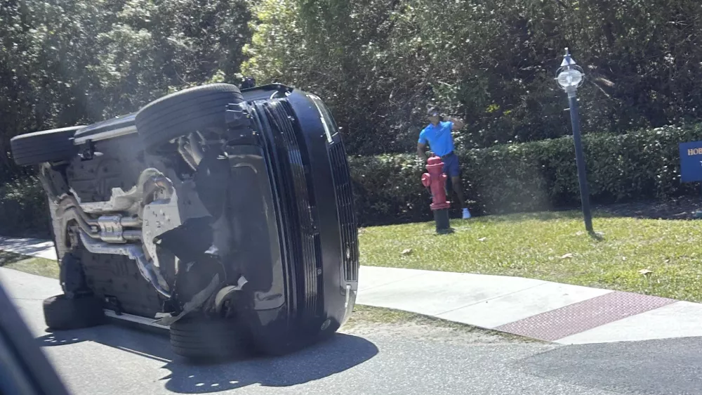 FILE- Golfer Tiger Woods stands by his overturned vehicle in Jupiter Island, Fla., March 27, 2026. (AP Photo/Jason Oteri, File)