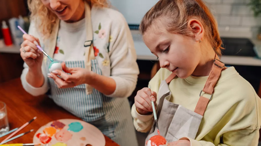 Mother and daughter sharing joyful moments, painting and decorating vibrant easter eggs with colorful paints in their cozy kitchen, creating cherished holiday memories together