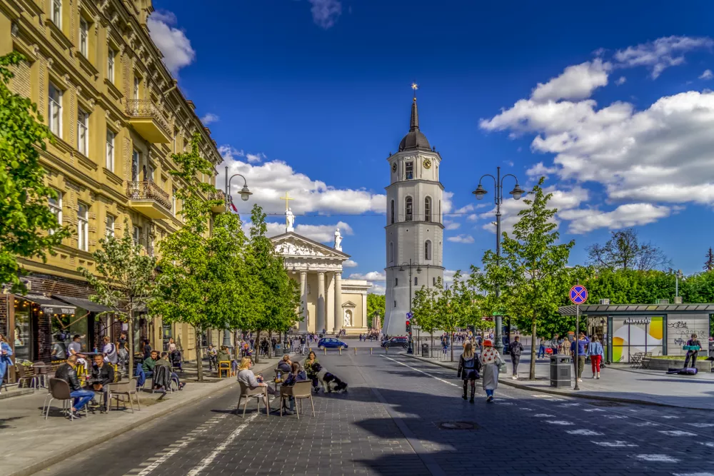 Vilnius, Lithuania - May 30, 2021: View to main Vilnius city street - Gedimino avenue, Vilnius Cathedral and bell tower with people walking and riding bike in sunny day.