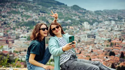 Two cheerful traveler girls in dark glasses are having fun and taking pictures against the background of Sarajevo, a beautiful European city in the mountains.