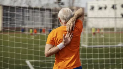 Rear view of senior sportsman standing on stadium and stretching his arms.