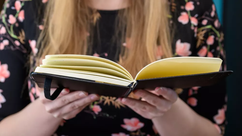 Young blonde girl with an open book in her hand, reading a book