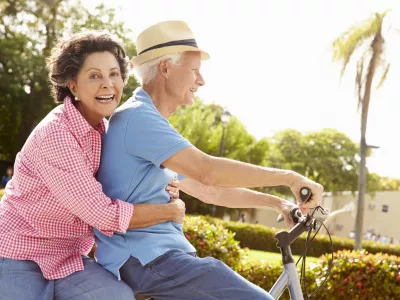 Senior Hispanic Couple Riding Bikes In Park Smiling To Camera