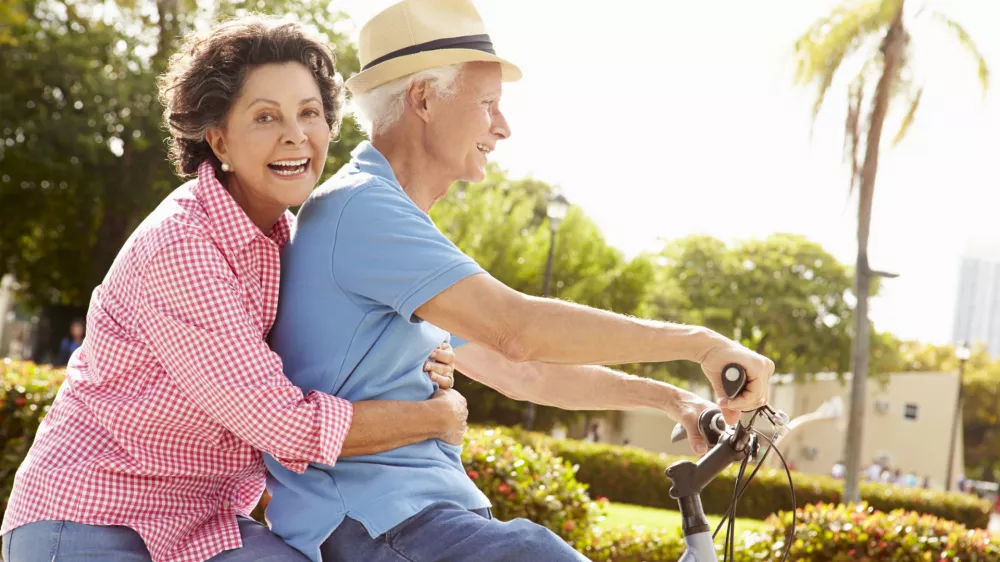 Senior Hispanic Couple Riding Bikes In Park Smiling To Camera