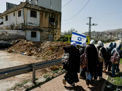 People walk past a newly installed dirt barrier by the Israeli military at the main entrance to Luban e-Sharkiya, between Nablus and Ramallah, in the Israeli-occupied West Bank, February 16, 2026. REUTERS/Ammar Awad