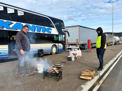 A man prepares to cook on a portable grill next to a line of trucks and buses on the Bosnian side of the border with Croatia, in Svilaj, Bosnia, Monday, Jan. 26, 2026, as drivers across the Balkans blocked dozens of border crossings in the region in protest over newly introduced European Union entry regulations.(AP Photo/Eldar Emric)