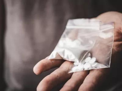 Man's hand holds two transparent plastic packets with cocaine powder and white pills lsd, drug dealer selling drugs. Drug abuse and addiction concept.