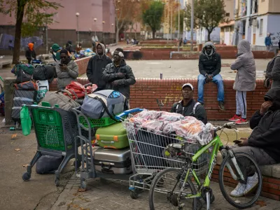 FILE - Migrants sit together with their belongings after being evicted by police from an abandoned school where they had been living in Badalona, near Barcelona, Spain, Wednesday, Dec. 17, 2025. (AP Photo/Emilio Morenatti, File)