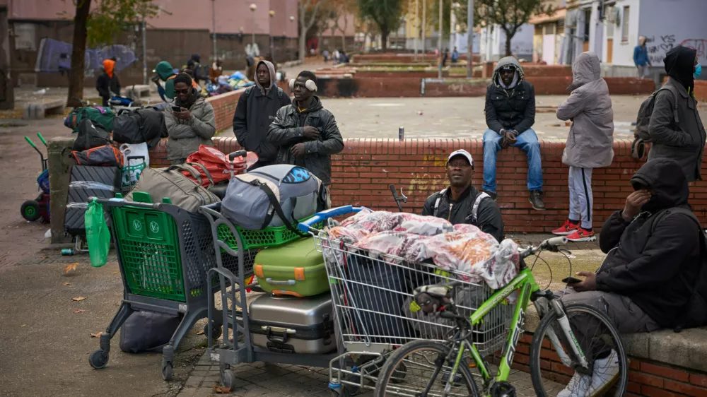 FILE - Migrants sit together with their belongings after being evicted by police from an abandoned school where they had been living in Badalona, near Barcelona, Spain, Wednesday, Dec. 17, 2025. (AP Photo/Emilio Morenatti, File)