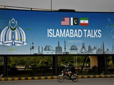FILE PHOTO: A man rides his motorbike past a billboard installed alongside a road as Pakistan prepares to host the U.S. and Iran for peace talks, in Islamabad, Pakistan, April 10, 2026. REUTERS/Waseem Khan/File Photo