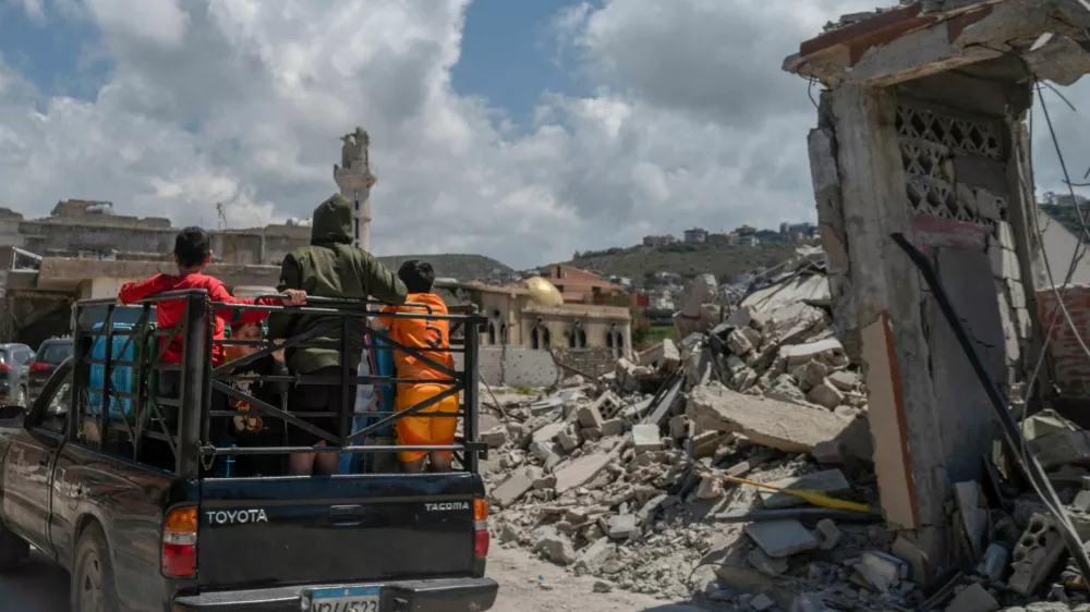 Children stand on a pick-up as they ride past buildings damaged by an Israeli strike in Mansouri village, southern Lebanon, amid a 10-day ceasefire between Lebanon and Israel, April 21, 2026. REUTERS/Zohra Bensemra