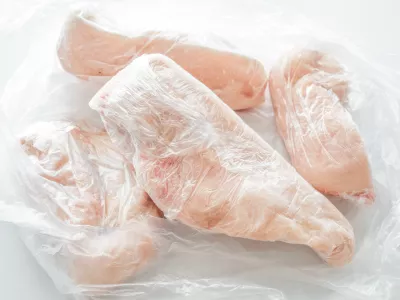 Frozen chicken breast in food plastic wrap or cling film. Photo can be used for how to wrap meat for freezer concept.