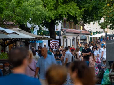 Capturing the lively atmosphere of a European summer, this shot shows a bustling pedestrian street in Ljubljana's historic center. Crowds of tourists and locals stroll past outdoor cafes and shops shaded by large trees. The warm natural light and vibrant urban energy make it ideal for travel guides, city lifestyle features, and tourism marketing showcasing popular destinations in Slovenia. / Foto: Aleksei Gorovoi Getty Images