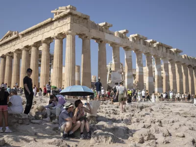 A tourist drinks water as she and a man sit under an umbrella in front of the five century BC Parthenon temple at the Acropolis hill during a heat wave, on Thursday, July 13, 2023. The government has announced emergency measures this week, allowing workers to stay home during peak temperature hours as a heat wave is due to affects most of Greece. (AP Photo/Petros Giannakouris)