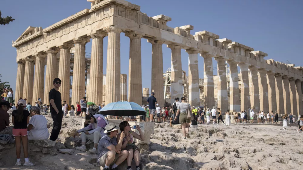 A tourist drinks water as she and a man sit under an umbrella in front of the five century BC Parthenon temple at the Acropolis hill during a heat wave, on Thursday, July 13, 2023. The government has announced emergency measures this week, allowing workers to stay home during peak temperature hours as a heat wave is due to affects most of Greece. (AP Photo/Petros Giannakouris)