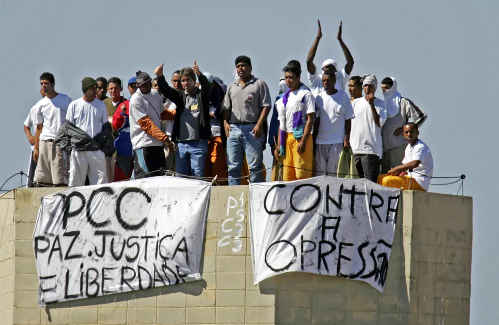 Gang members of the First Capital Command, known by its Portuguese initials PCC, hold a riot on top of the Junqueiropolis penitentiary in Sao Paulo state, Brazil, May 14, 2006. The signs read: "PCC, peace, justice and liberty," left, and "against oppression," right. Authorities acknowledge that PCC, controls life inside about 80 percent of Sao Paulo prisons, with smaller ones ruling the rest. And experts say that until their clout behind bars is broken, they won't lose their power on the streets either. (AP Photo/Alex Silva, Agencia Estado) ** BRAZIL OUT **