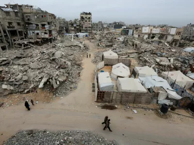 Palestinians walk past the rubble of residential buildings destroyed during the two-year Israeli offensive, in Khan Younis, southern Gaza Strip, April 15, 2026. REUTERS/Ramadan Abed