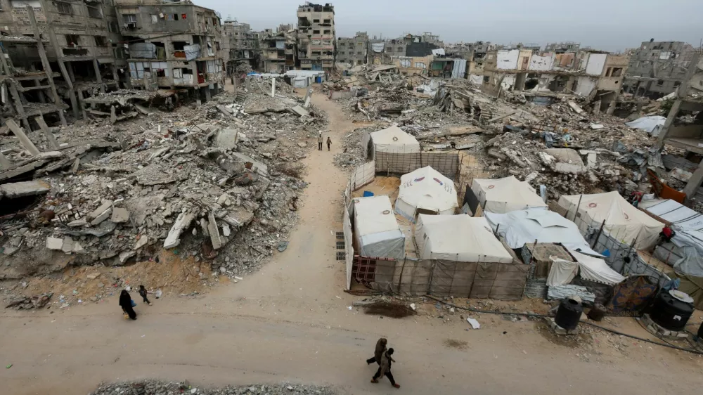 Palestinians walk past the rubble of residential buildings destroyed during the two-year Israeli offensive, in Khan Younis, southern Gaza Strip, April 15, 2026. REUTERS/Ramadan Abed