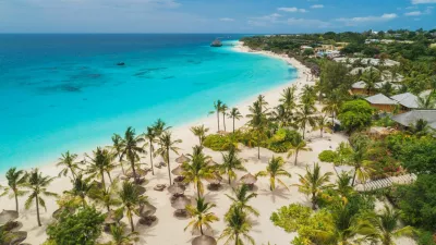 Aerial view of palms on the sandy beach of Indian Ocean at sunny day. Summer holiday in Zanzibar, Africa. Tropical landscape with palm trees, white sand, blue water, hotels. Top view of sea coast / Foto: Den-belitsky