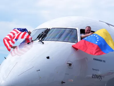 Capt. Ric Wilson waves a Venezuelan flag and the first officer waves a U.S. flag as they prepare to fly American Airlines Flight AA3599, the first direct commercial flight between the United States and Venezuela in seven years, Thursday, April 30, 2026, at Miami International Airport in Miami. (AP Photo/Rebecca Blackwell)