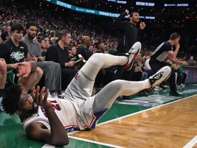 Philadelphia 76ers' Joel Embiid dives onto the ground in pursuit of a loose ball in front of the Boston Celtics bench late in the fourth quarter. Celtics head Joe Mazzulla is standing in the center, while injured Celtics player Jayson Tatum (in grey at left) looks on during Game 7 of a first round NBA basketball playoffs series, Saturday, May 2, 2026 in Boston. (AP Photo/Jim Davis)