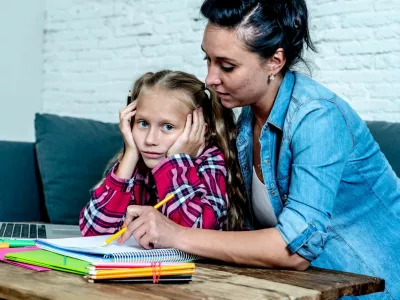Mother becoming frustrated with daughter whilst doing homework sitting on sofa At home in learning difficulties homework parenting and education concept