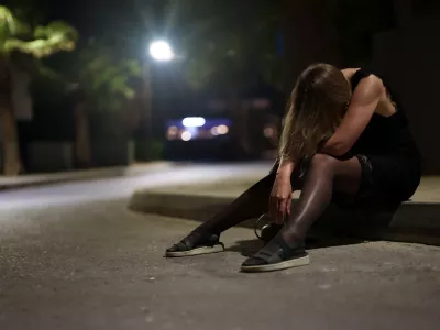Drunk woman in dress sits on the roadside at night.