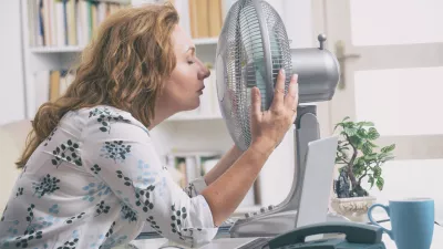 Woman suffers from heat while working in the office and tries to cool off by the fan