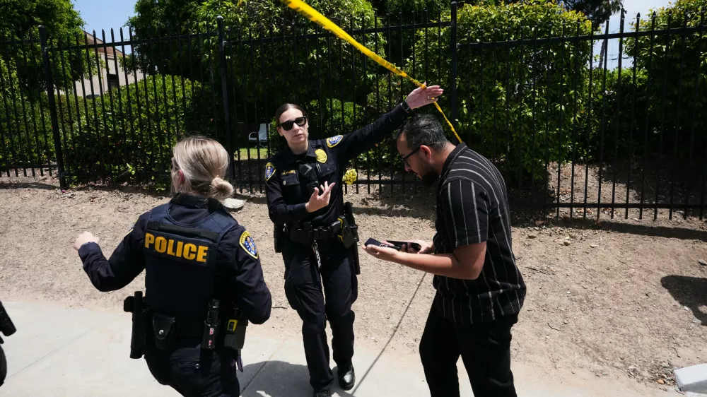 People walk under police tape at the scene of a shooting outside the Islamic Center of San Diego Monday, May 18, 2026, in San Diego. (AP Photo/Gregory Bull)