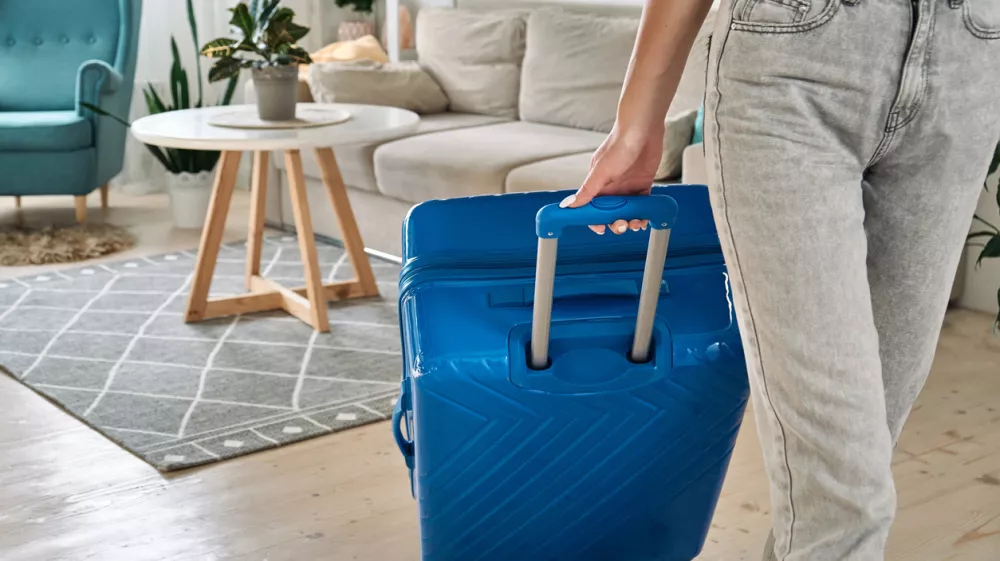 Unrecognizable woman leaving home with a suitcase going on a trip or vacation.