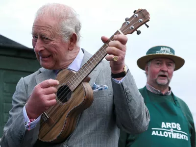 Britain's King Charles plays ukulele as the founder of Ards Allotments, Maurice Patton, looks on during his visit to Ards Allotments, in County Down, Northern Ireland, May 21, 2026. REUTERS/Toby Melville/Pool