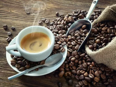 Cup of espresso with coffee beans, bag, scoop and steam on rustic wooden background