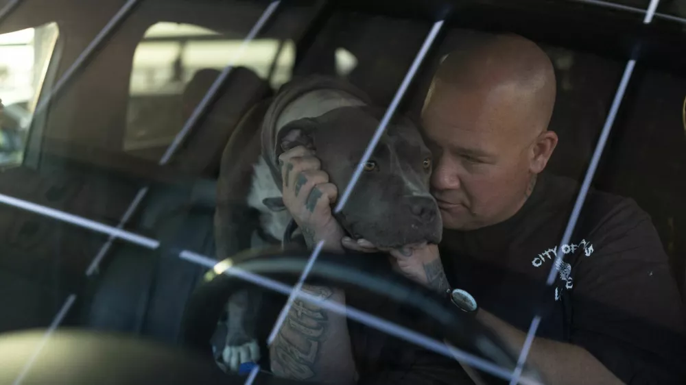 Kevin Hatch of Garden Grove sits in his car with his dog, Smokey, outside the Ocean View High School gymnasium, which was converted into a temporary shelter after nearby residents were ordered to evacuate because of a failing tank containing methyl methacrylate, a flammable liquid used in the aerospace industry, in Huntington Beach, California, on May 23, 2026. REUTERS/Ed Ou
