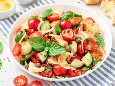 Panzanella - Italian salad from vegetables and bread. Salad with tomatoes, onions, cucumbers, bread, capers and basil in a white plate on a gray concrete background. Vegan salad, Italian cuisine / Foto: Svetlana Monyakova