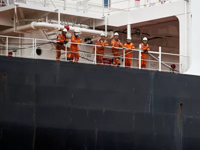 Six ship crew members wearing orange safety jumpsuits and hard hats posing together on the deck of a large vessel, Port of Gdansk, Pomerania, Poland, Europe. / Foto: Sebastian Gora Getty Images